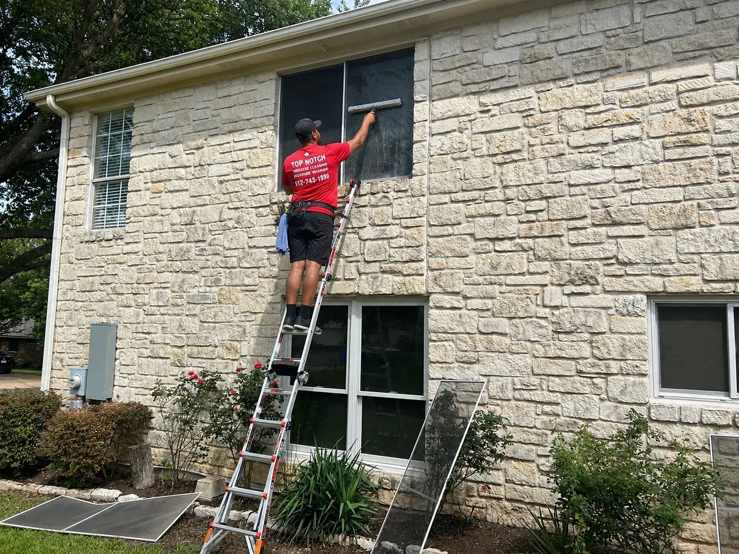 Top Notch Window Cleaning technician cleaning second-story residential window in Austin TX